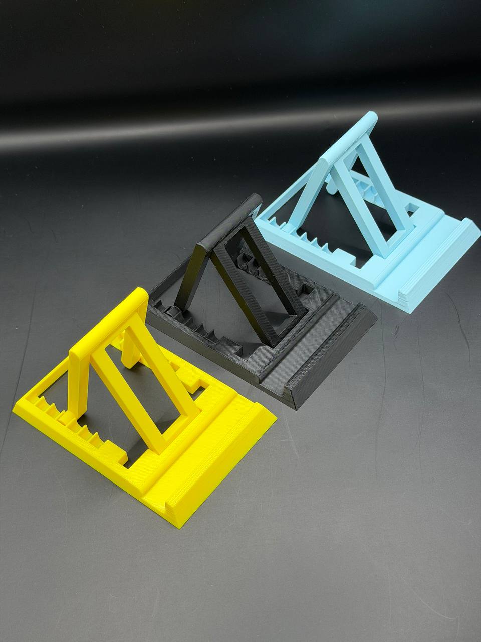 3D printed phone stands in yellow, black, and blue